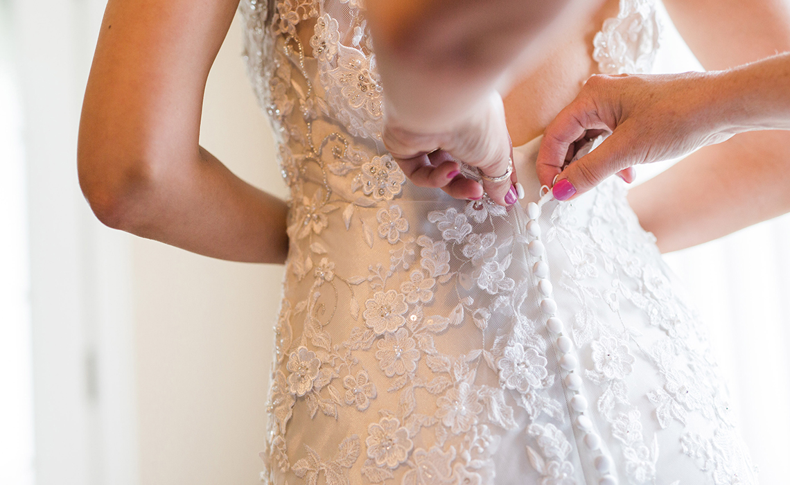 The Bride's dress is being buttoned by her loving mother the morning of her wedding