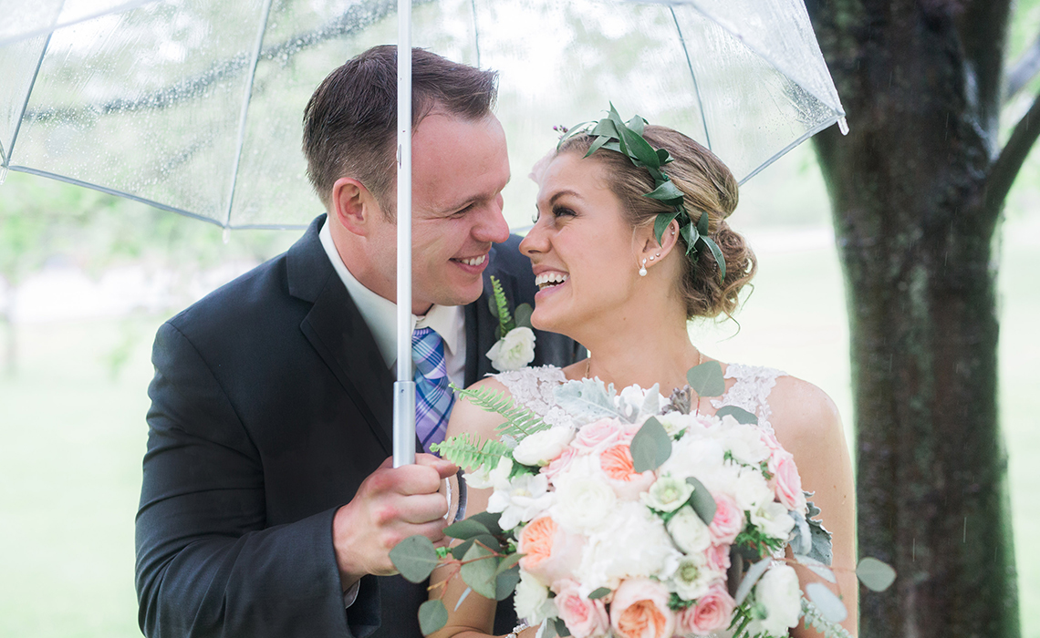 Maureen & Dave hide under an umbrella on their rainy wedding day